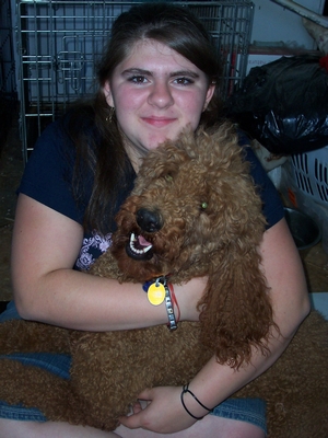 A young woman smiling while holding a curly brown dog.