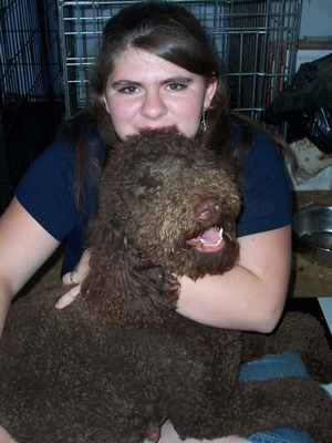 A young woman hugging a large, curly-coated brown dog.